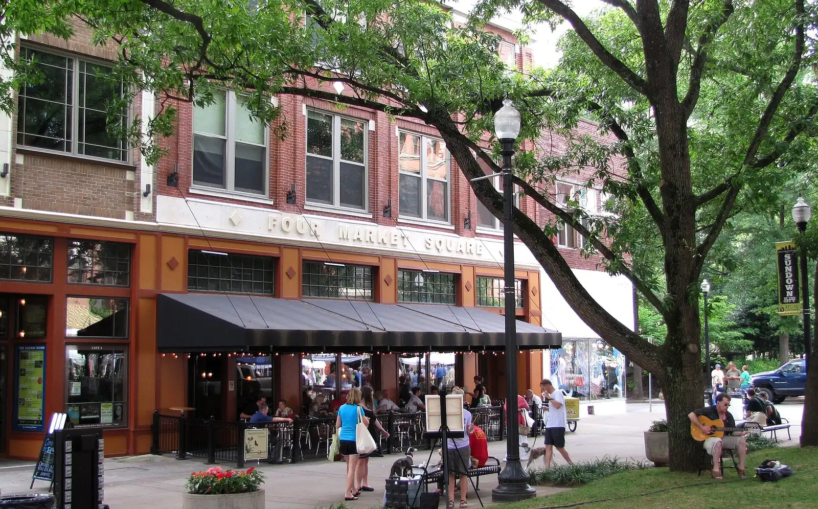 Diners on the patio of Cafe 4 at Four Market Square in downtown Knoxville, with a street musician under the oaks.