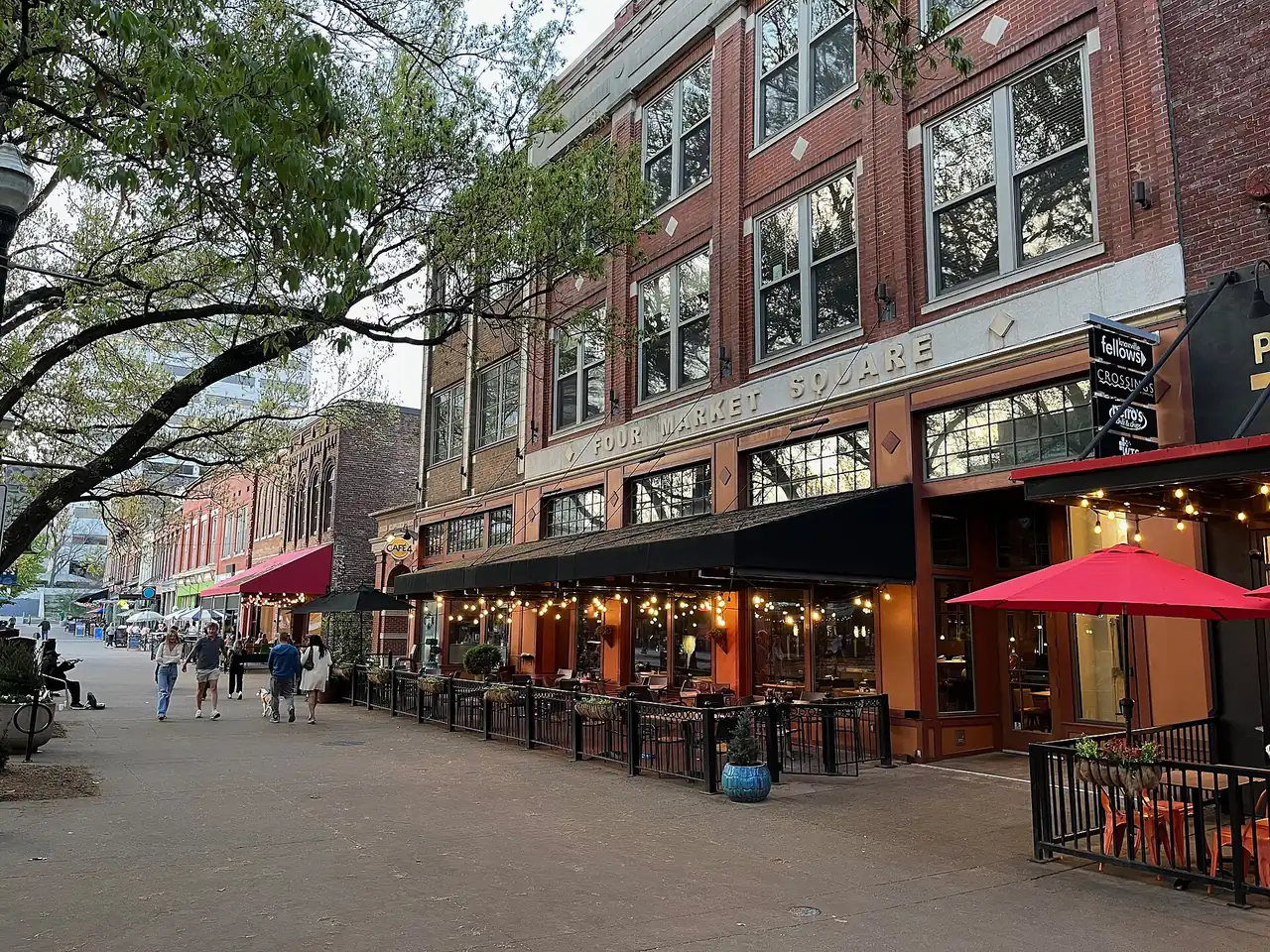 Fenced outdoor dining under string lights and red umbrellas in front of Four Market Square on Market Square in downtown Knoxville.